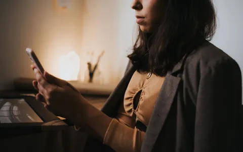 Mulher com o corpo tenso olhando para o celular em ambiente de trabalho