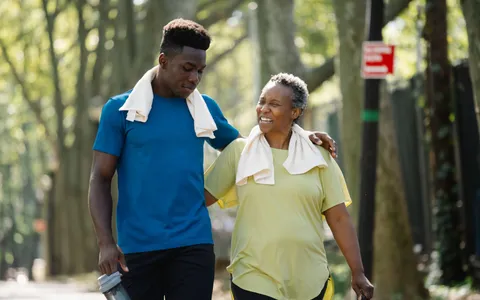 Jovem e mulher mais velha caminhando juntos em um parque arborizado depois de se exercitar