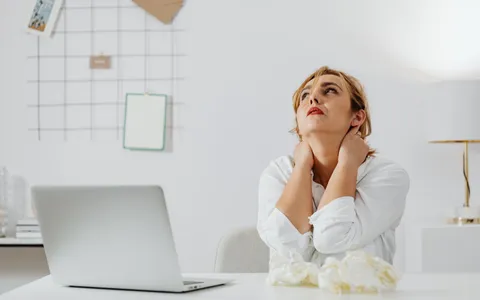 Pessoa sentada em mesa de trabalho segurando a região lombar com expressão de desconforto