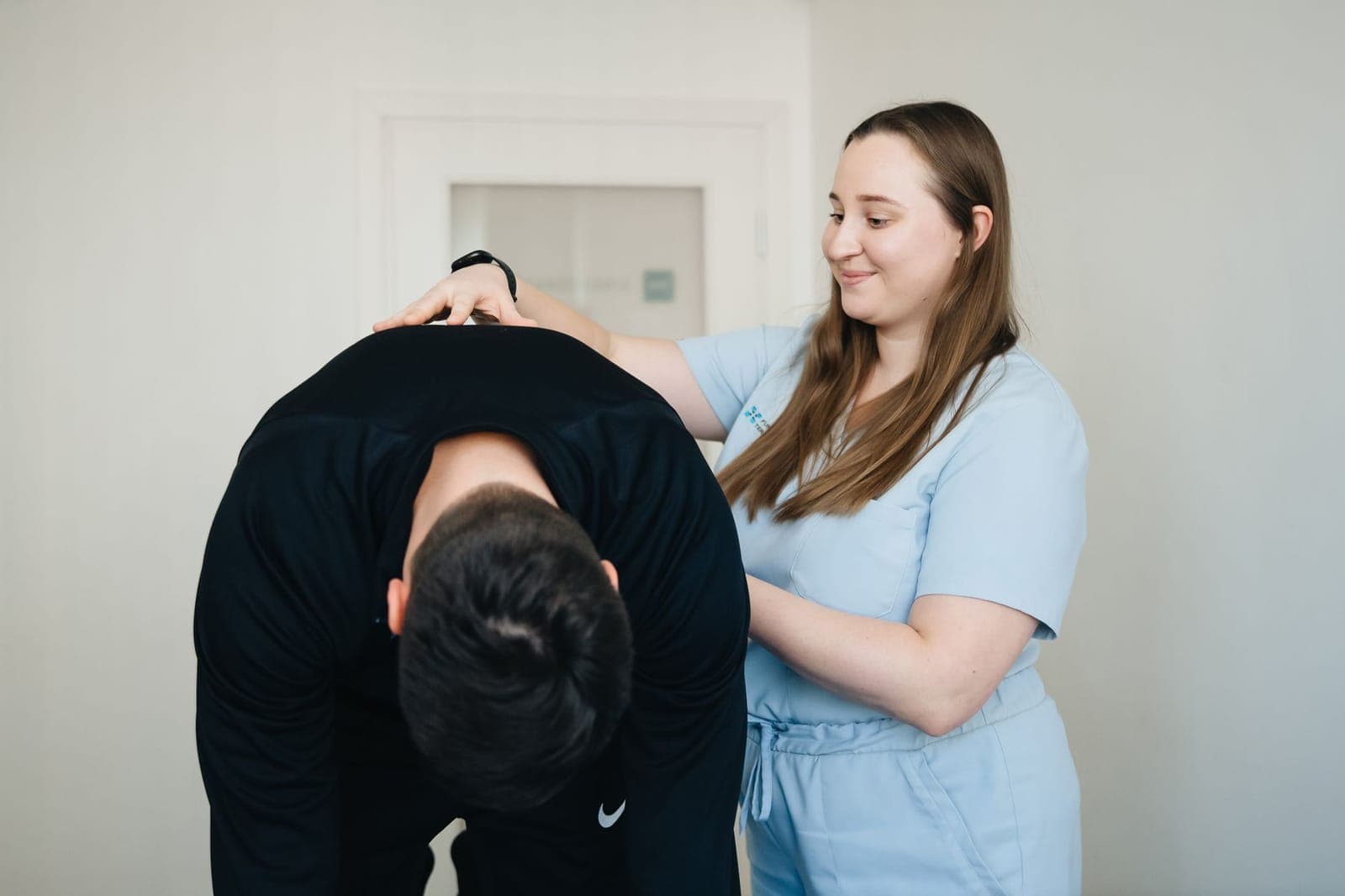 Fisioterapeuta avaliando a mobilidade da coluna cervical e do ombro de um paciente em consultório