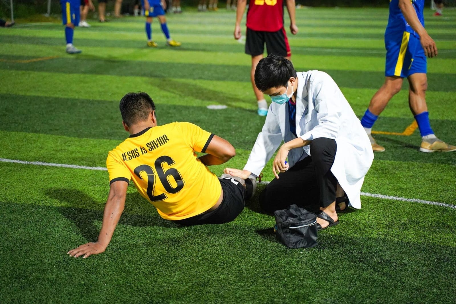 Atleta sentado no gramado segurando a parte posterior da coxa após uma lesão