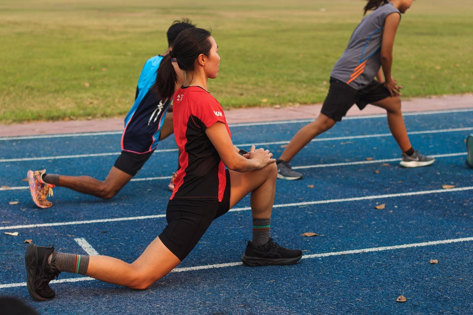 Grupo de corredores alongando a perna em pista de atletismo antes do treino
