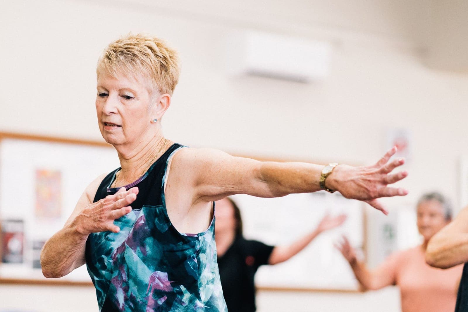 Mulher mais velha praticando exercício em grupo, com os braços estendidos para os lados
