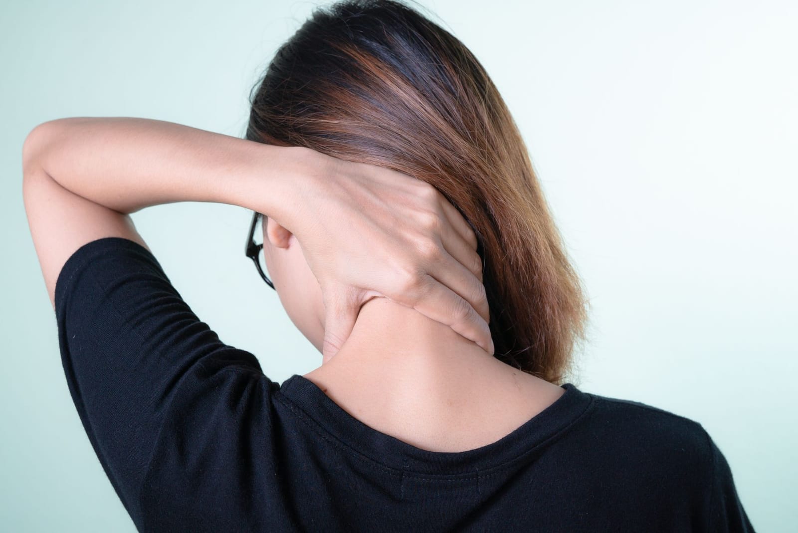 Mulher levando a mão à nuca, sentindo rigidez na região cervical