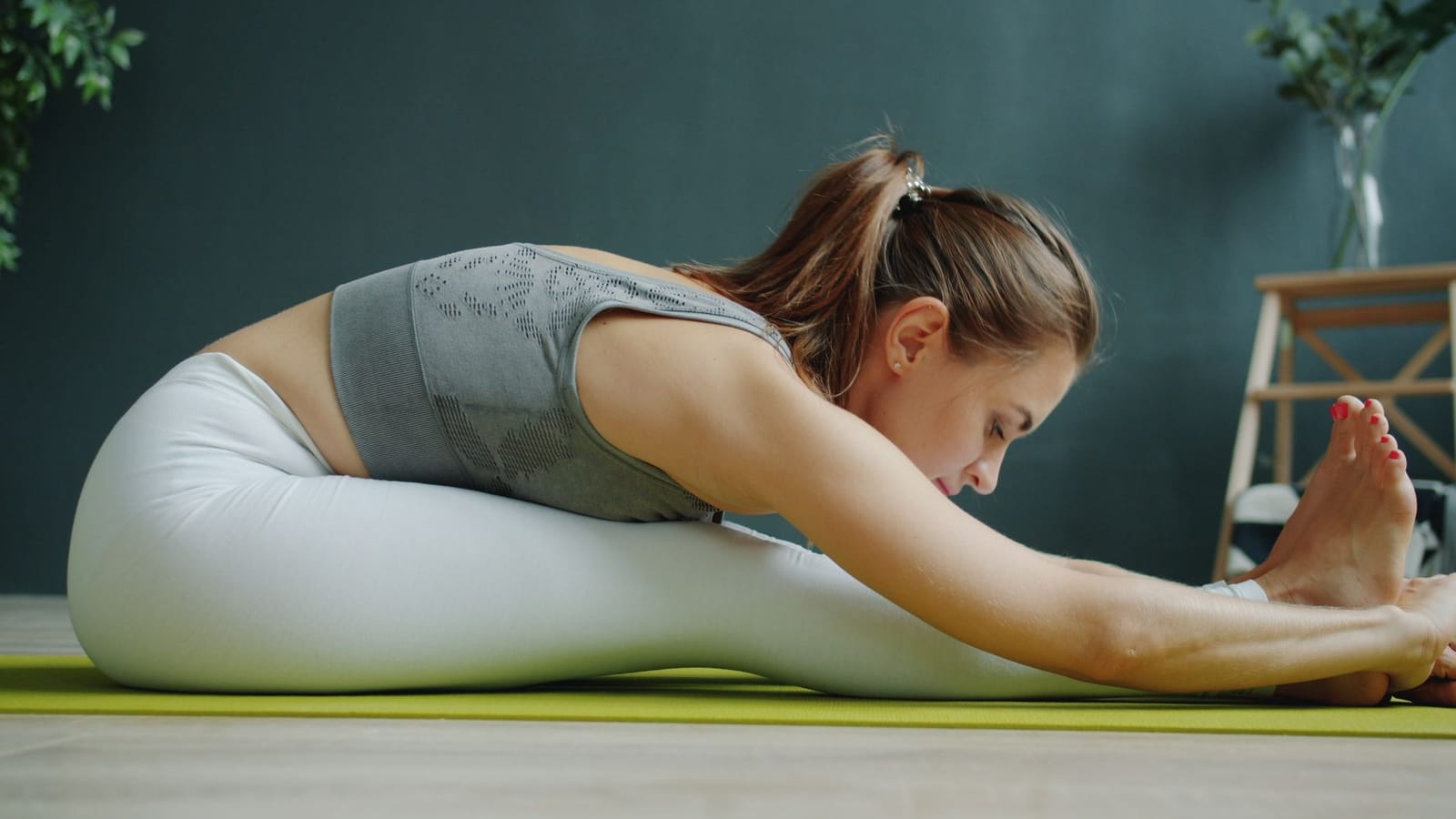 Mulher sentada em posição de alongamento, flexionando o tronco à frente com os braços estendidos