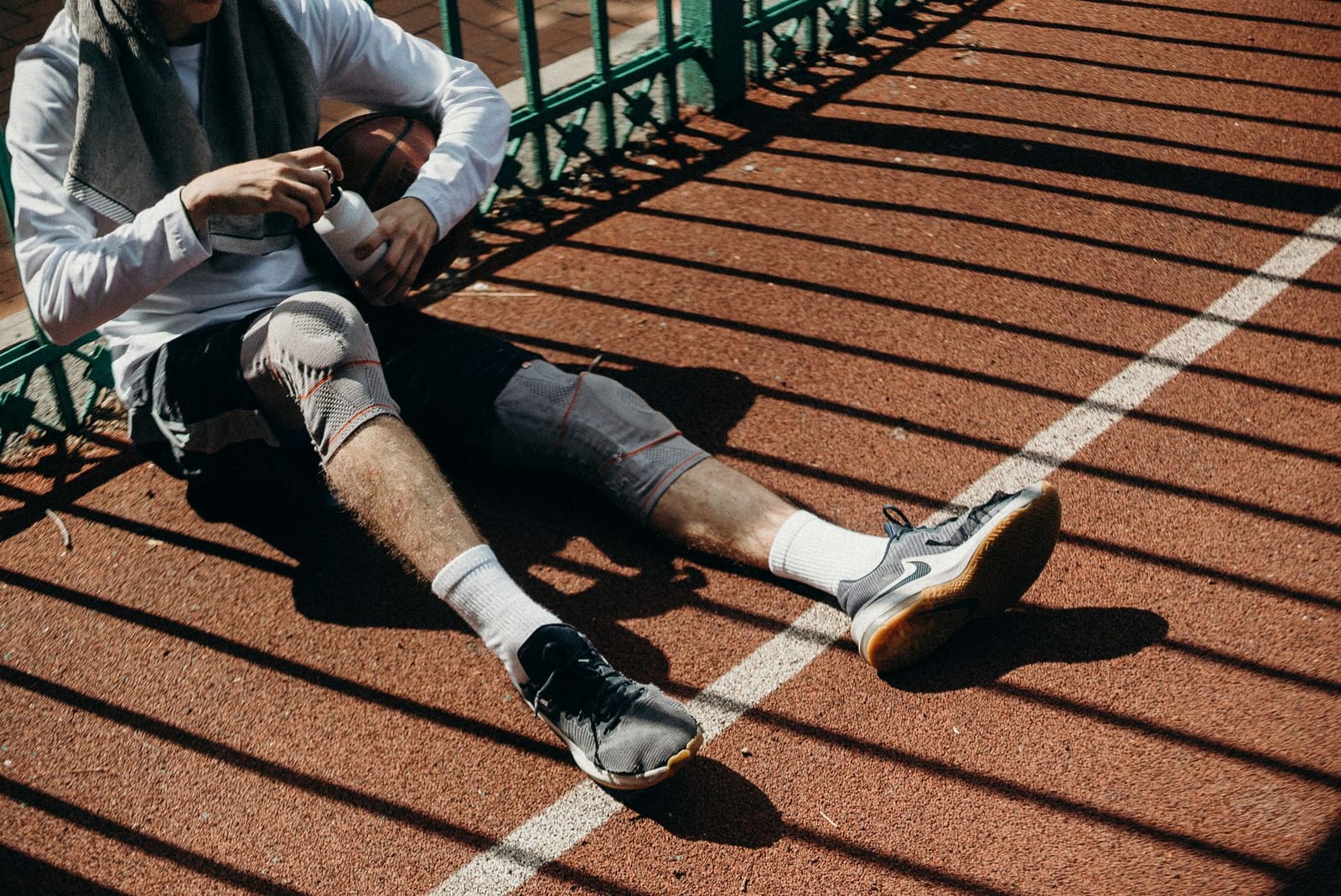 Atleta sentado em uma pista, usando joelheira elástica, descansando após a atividade física